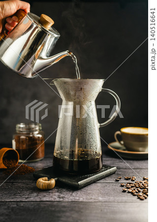 Pour hot water over coffee brewing with dripper and kettle, specialty coffee preparation, dark background, still life Pour hot water over coffee brewing with dripper and kettle, specialty coffee preparation, dark background, still life 140516641