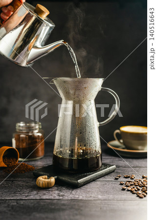 Pour hot water over coffee brewing with dripper and kettle, specialty coffee preparation, dark background, still life Pour hot water over coffee brewing with dripper and kettle, specialty coffee preparation, dark background, still life 140516643