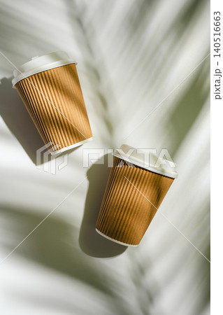 Two takeaway coffee cups with palm leaf shadows on white background, flat lay with copy space Two takeaway coffee cups with palm leaf shadows on white background, flat lay with copy space 140516663