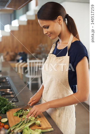 Woman, knife and vegetables in home kitchen with smile, apron and cooking for healthy nutrition for dinner. Girl, person and meal prep with vegan diet for health food, wellness and lunch in apartment 140517259