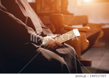A monk in robes with holy bible in their hands praying in the church A monk in robes with holy bible in their hands praying in the church 140517307