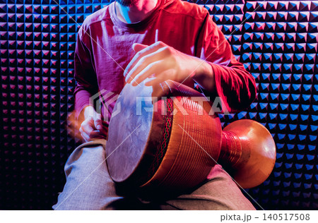 Young man playing on djembe in sound recording studio. Young man playing on djembe in sound recording studio. 140517508
