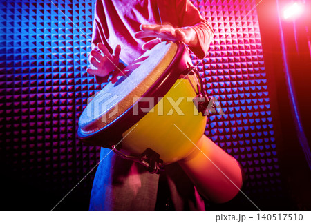 Young man playing on djembe in sound recording studio. Young man playing on djembe in sound recording studio. 140517510