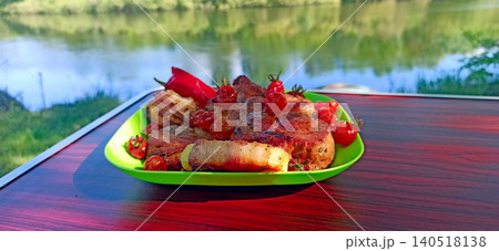 Grilled meat and bacon wrapped potatoes served with cherry tomatoes near a river Grilled meat and bacon wrapped potatoes served with cherry tomatoes near a river 140518138