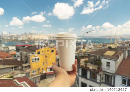 Hand holding white takeaway coffee cup against panoramic skyline of Istanbul, Turkey. Blurred cityscape, Bosphorus Strait, rooftops, blue sky create vibrant travel and lifestyle scene. Hand holding white takeaway coffee cup against panoramic skyline of Istanbul, Turkey. Blurred cityscape, Bosphorus Strait, rooftops, blue sky create vibrant travel and lifestyle scene. 140518427