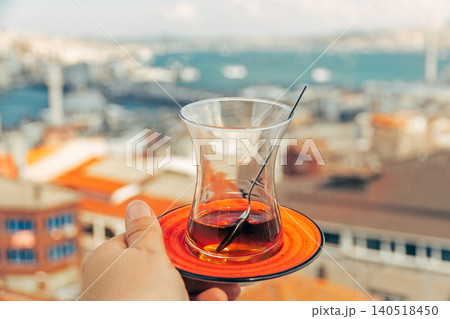 One fresh tea in Turkish teacup Armudu at bottom in woman's palm against backdrop of cityscape sunny Istanbul 140518450