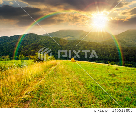 sunset over rural field on the hill. view in to the valley. countryside mountain landscape. alpine pasture near forested hills. timeless nostalgia book cover with rainbow 140518800