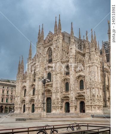 Milan, italy, october 2, 2024. Milan cathedral, a landmark of gothic architecture, standing prominently in an empty city square on a cloudy autumn day 140518981
