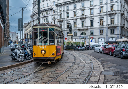 Milan, italy, october 2, 2024. Historic yellow tram running on cobblestone tracks through a busy milan city street with parked scooters, cars, and people Milan, italy, october 2, 2024. Historic yellow tram running on cobblestone tracks through a busy milan city street with parked scooters, cars, and people 140518994