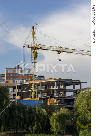 Large yellow crane next to a modern high-rise building under construction against a blue sky Large yellow crane next to a modern high-rise building under construction against a blue sky 140519168