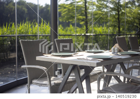 Served restaurant table on terrace with wicker chairs and scenic nature view Served restaurant table on terrace with wicker chairs and scenic nature view 140519230
