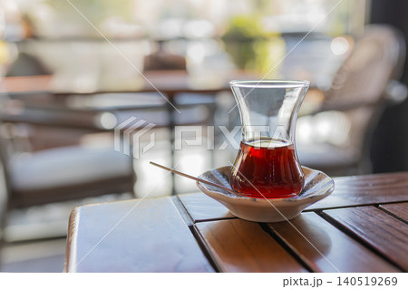 One half-empty Turkish teacup Armudu with fresh tea stands in saucer on wooden table in cafe against bokeh background 140519269