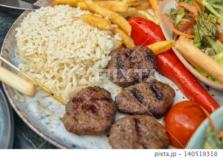 Close-up of traditional Turkish grilled meatballs served with rice pilaf, French fries, grilled vegetables and fresh salad on plate. Authentic Turkish cuisine meal in restaurant 140519318