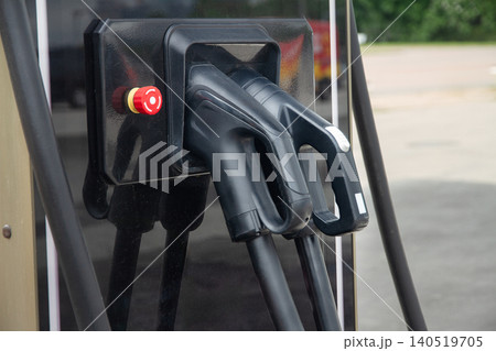 Close up view of two black electric vehicle EV charging plugs and an emergency stop button inserted into a public charging station dock 140519705