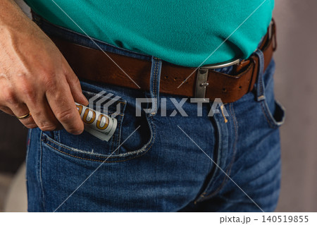 Man placing money in pocket of jeans while standing indoors Man placing money in pocket of jeans while standing indoors 140519855