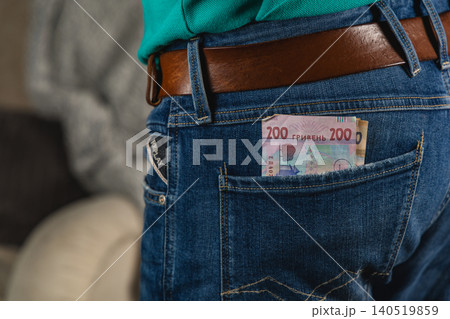 Man stands with cash in his back pocket while wearing blue jeans Man stands with cash in his back pocket while wearing blue jeans 140519859