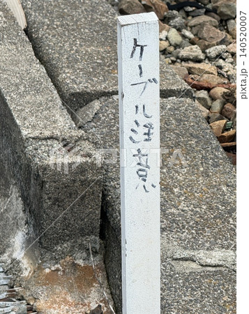 線路脇にある「ケーブル注意」の手書きの白い木杭 線路脇にある「ケーブル注意」の手書きの白い木杭 140520007