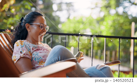 Latina woman relaxing on balcony using smartphone Latina woman relaxing on balcony using smartphone 140520521