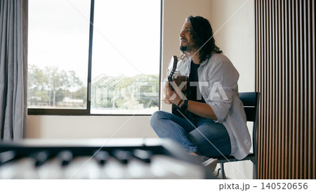 Man playing acoustic guitar by window at home Man playing acoustic guitar by window at home 140520656
