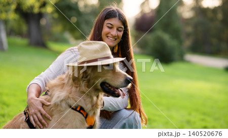 Woman smiling with golden retriever wearing hat in park Woman smiling with golden retriever wearing hat in park 140520676