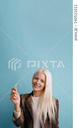 Woman smiling, holding clear plastic dental aligner 140521011