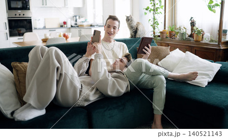 Gay couple relaxing on sofa with smartphone and cat Gay couple relaxing on sofa with smartphone and cat 140521143