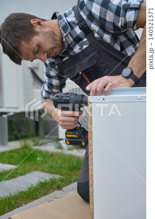 Man secures drawer side with cordless drill while holding the panel steady outdoors Man secures drawer side with cordless drill while holding the panel steady outdoors 140521371