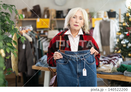 Uncertain mature woman choosing jeans pantaloons in clothing store Uncertain mature woman choosing jeans pantaloons in clothing store 140522200