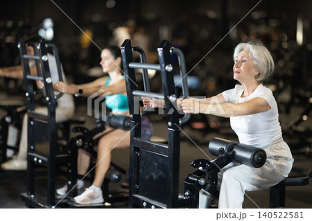 Senior woman performing resistance sit-to-stand leg exercise in gym Senior woman performing resistance sit-to-stand leg exercise in gym 140522581