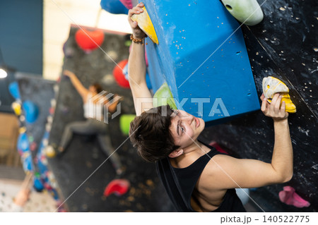 Confident young man scaling artificial climbing wall in climbing gym Confident young man scaling artificial climbing wall in climbing gym 140522775