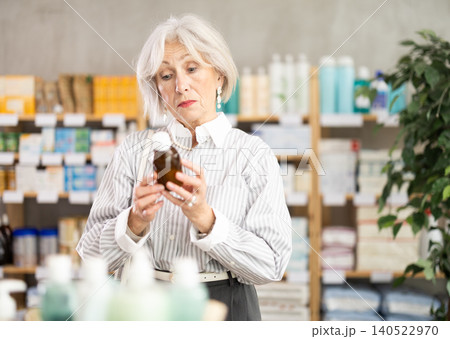 Mature woman in summer clothes choosing medicinal cough syrup at pharmacy 140522970