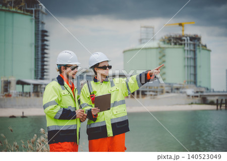 Field engineers in high visibility jackets pointing and discussing at coastal oil facility Field engineers in high visibility jackets pointing and discussing at coastal oil facility 140523049