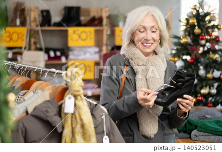 Positive old lady choosing heeled ankle boots in clothing store Positive old lady choosing heeled ankle boots in clothing store 140523051