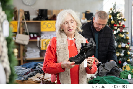 Mature woman choosing heeled boots in Christmas shop Mature woman choosing heeled boots in Christmas shop 140523099