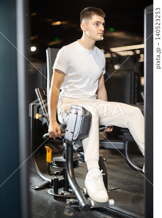 In gym, guy uses gym apparatus to strengthen leg muscles In gym, guy uses gym apparatus to strengthen leg muscles 140523253