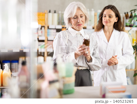 Mature woman choose antitussive syrup, woman pharmacist offers similar item 140523265
