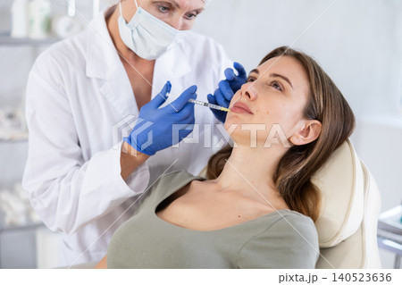 Beautician makeing cosmetic injection in the lips. Woman gets filler injection in her face. Beautician makeing cosmetic injection in the lips. Woman gets filler injection in her face. 140523636