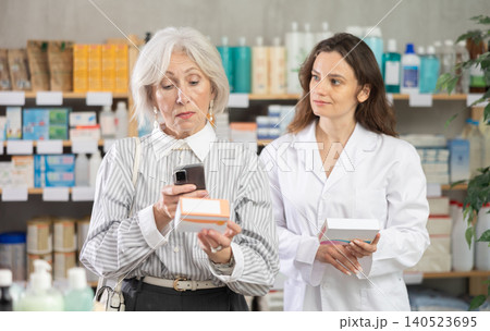 Elderly woman scans barcode of medicine package in front of pharmacist Elderly woman scans barcode of medicine package in front of pharmacist 140523695