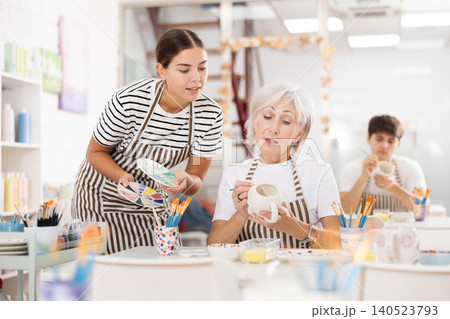 Young female ceramicist teaching elderly woman to paint ceramics in pottery studio Young female ceramicist teaching elderly woman to paint ceramics in pottery studio 140523793