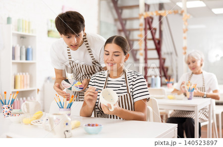 Young ceramicist teaching female novice art of ceramic painting in pottery studio 140523897