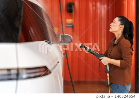 woman washing car with water hose in a self-service car wash station woman washing car with water hose in a self-service car wash station 140524654