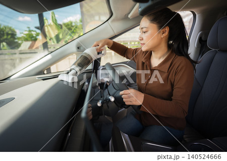 woman using portable handheld vacuum cleaner to clean dust on an electric car dashboard woman using portable handheld vacuum cleaner to clean dust on an electric car dashboard 140524666