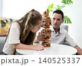 Father and daughter playing wooden block tower game at home. Family bonding activity, child development, learning through play, concentration, and positive parenting in a cozy living room. 140525337