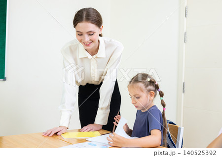 Teacher assisting young student with drawing and learning activity in classroom. Creative education, child development, personalized learning, and academic support concept. Teacher assisting young student with drawing and learning activity in classroom. Creative education, child development, personalized learning, and academic support concept. 140525392
