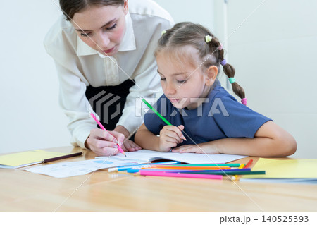 Teacher assisting young student with drawing and learning activity in classroom. Creative education, child development, personalized learning, and academic support concept. 140525393