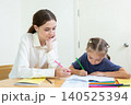 Teacher assisting young student with drawing and learning activity in classroom. Creative education, child development, personalized learning, and academic support concept. 140525394