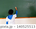 boy student writing on blank green chalkboard in classroom during lesson at school 140525513