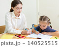 Teacher assisting young student with drawing and learning activity in classroom. Creative education, child development, personalized learning, and academic support concept. 140525515