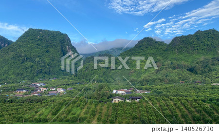 Panoramic view of lush green mountains covered by mist and low clouds above a rural village. Panoramic view of lush green mountains covered by mist and low clouds above a rural village. 140526710