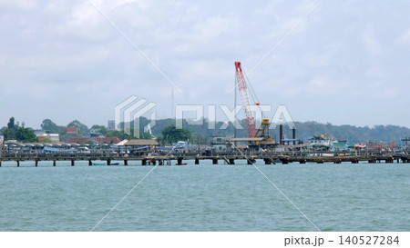 Industrial crane operating on the pier territory near the water with dock structures and calm sea visible in background. Port operations concept Industrial crane operating on the pier territory near the water with dock structures and calm sea visible in background. Port operations concept 140527284
